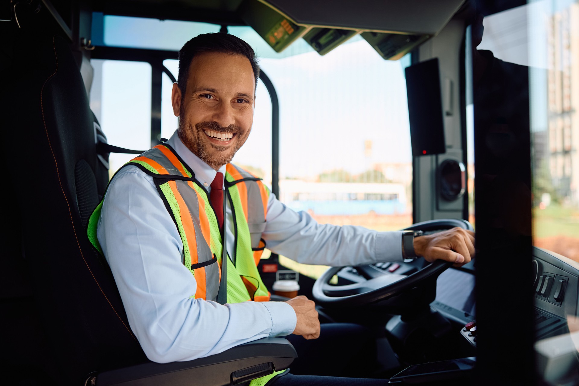 Happy public transport driver behind the wheel in bus cabin looking at camera.
