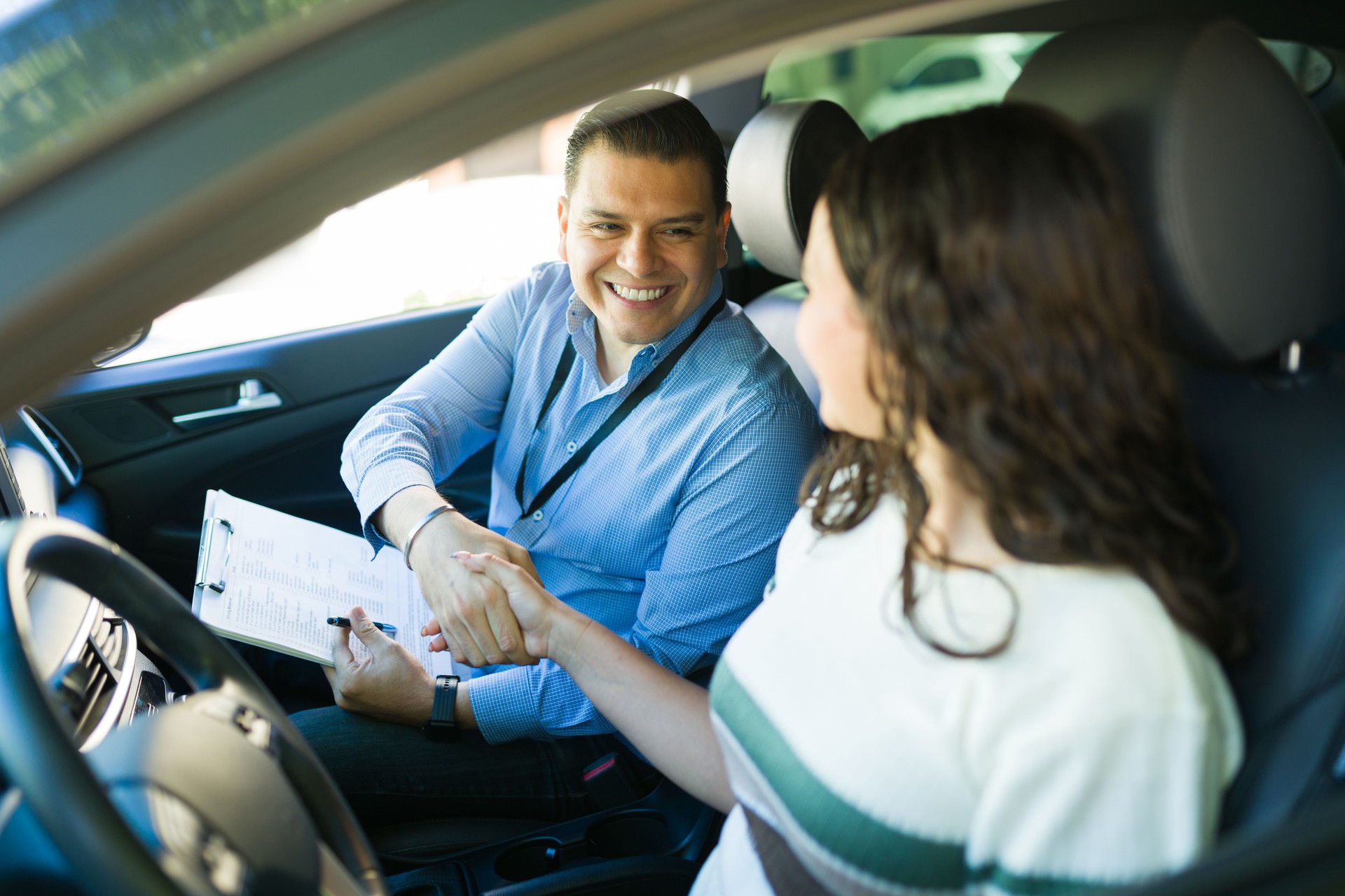 Happy driving instructor shaking hands with his student after passing the driving test inside a car